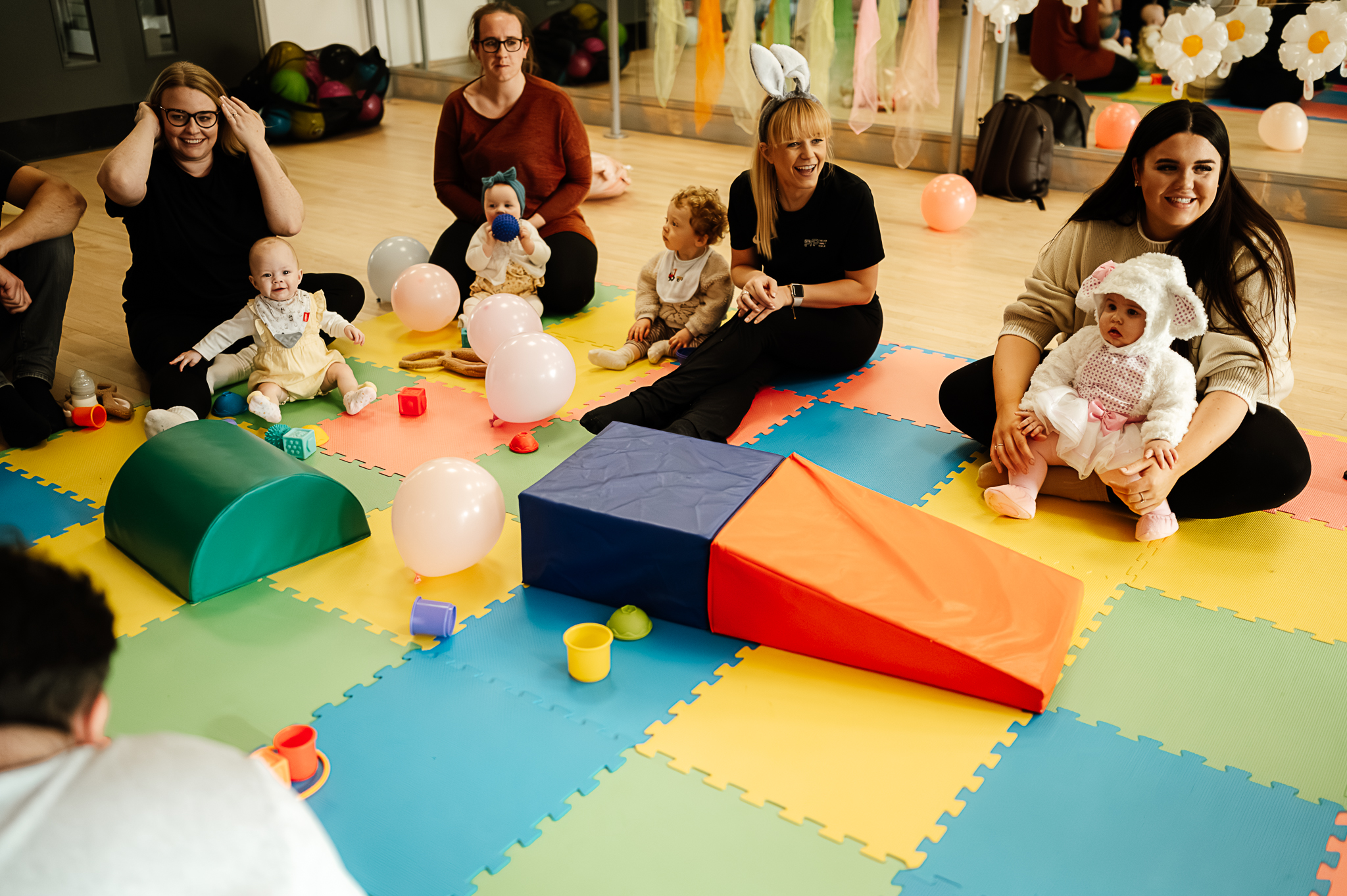 Young baby crawling at the Dots mum and baby class run by Forever Young People showing a playmat and various mothers with their baby