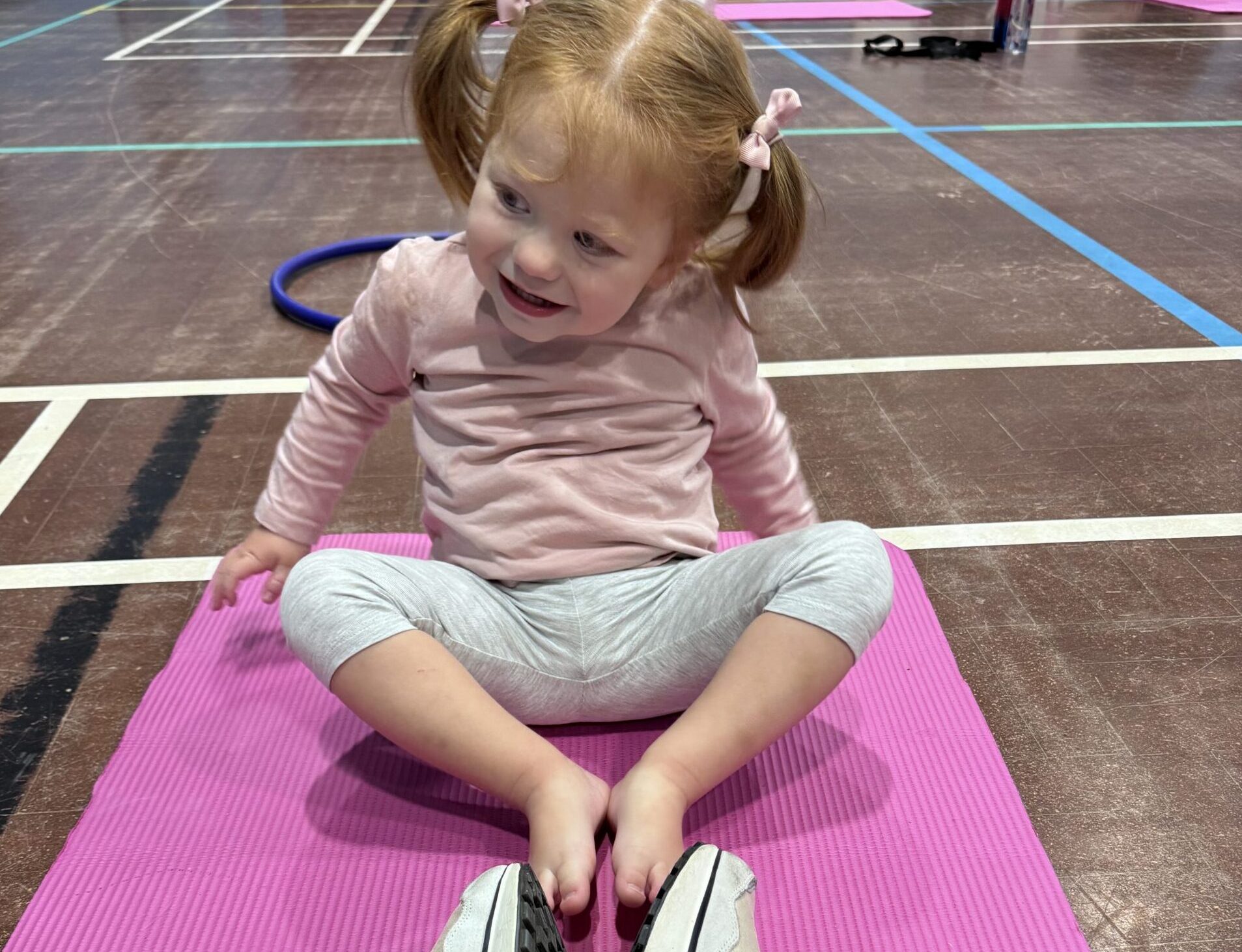 Dots mum and baby fitness class showing a little girl on a pink mat stretching with her parent